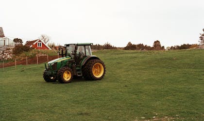 Grønn traktor med gule hjul på et jordet.