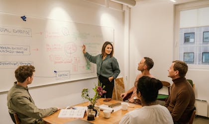 Kvinne presenterer noe på en tavle foran flere personer.