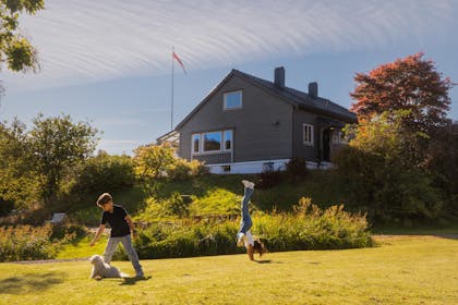 Barn som leker i solskinn på en stor grønn plen foran et hus.