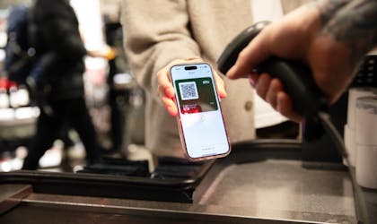 En person står i kassa for å betale og holder frem ID-kortet i BankID-appen. En annen person skanner QR-koden på ID-kortet.